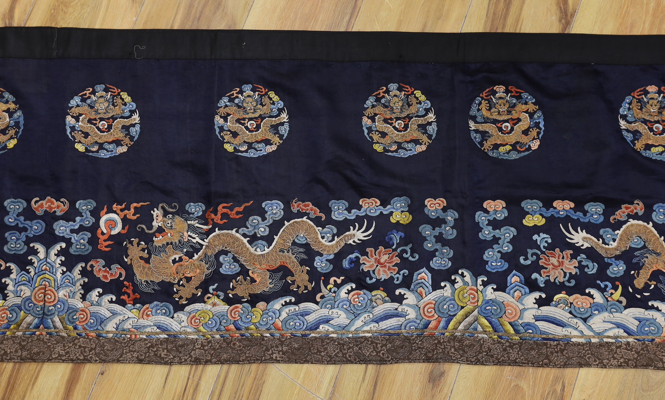 A Chinese long dark blue ground ‘dragon’ altar cloth, late Qing dynasty, polychrome embroidered, celestial dragons and mons amongst stylised clouds, 300 x 50cm